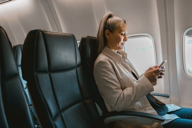 美丽的亚洲女性乘客坐在飞机上，在登机过程中使用手机图片下载