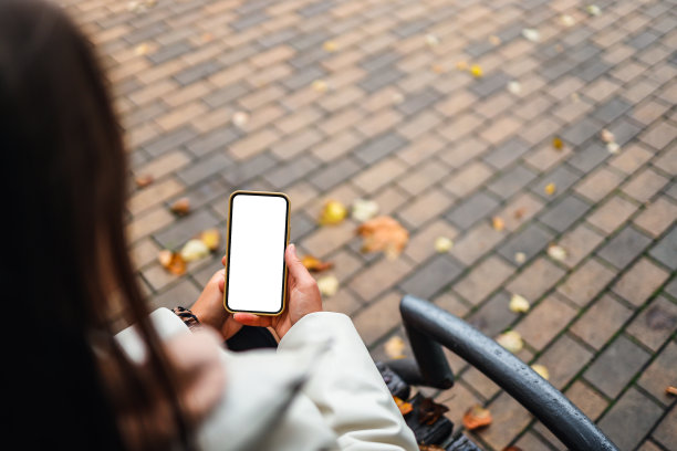 俯视图的一个女人的手拿着智能手机与白色的空白屏幕。复制空间在秋天的花园。女性用手机看文字和视频图片下载