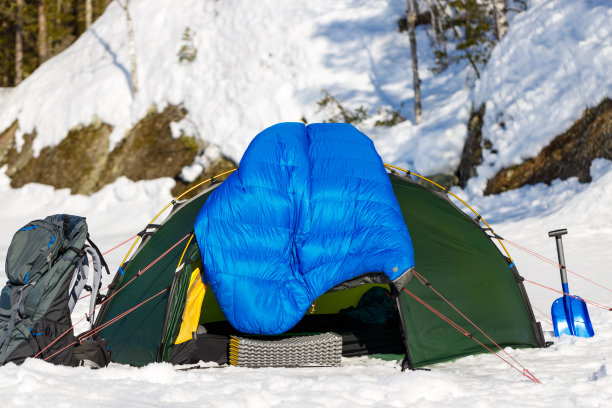 冬天的森林里，蓝色羽绒睡袋放在绿色的帐篷上晾干。图片下载