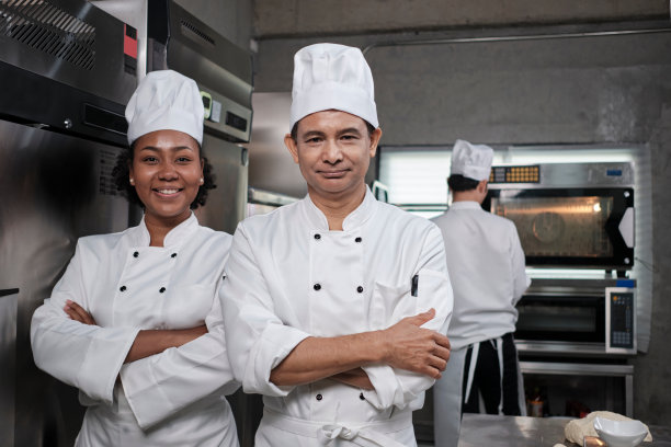 两个穿着制服的专业厨师在厨房里抱臂微笑。图片下载