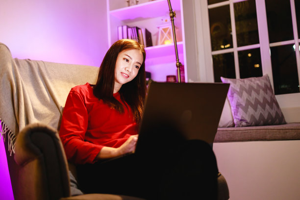 快乐的女人晚上在家里客厅的扶手椅上使用笔记本电脑图片下载