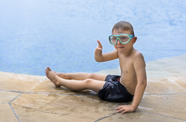 戴着泳镜的小男孩在室外游泳池里微笑。图片下载