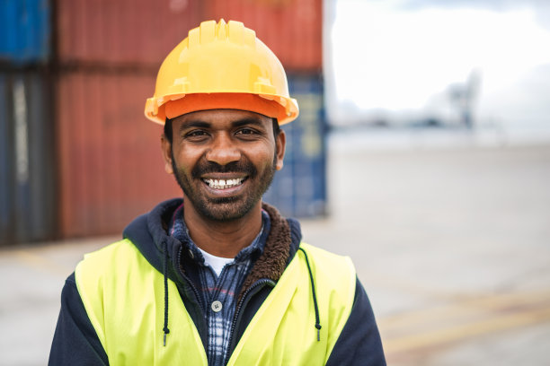 快乐的印度男子在镜头前微笑，背景是工业港口-关注面部图片下载