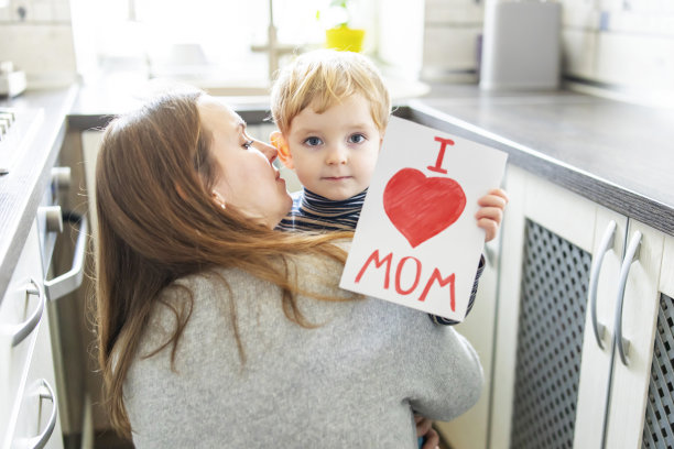 母亲节快乐!快乐的小男孩祝贺他的妈妈，并给她和红色的心画的贺卡图片下载