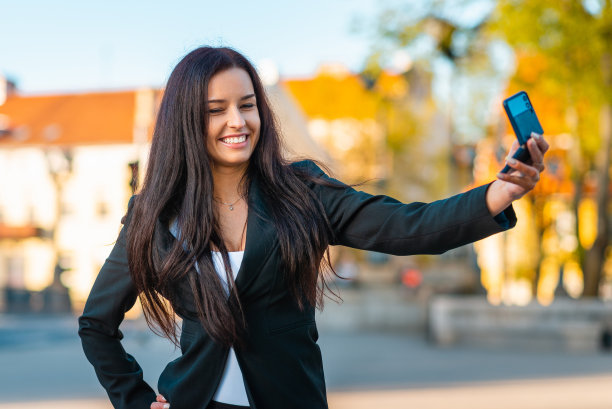一个年轻美丽的女商人的肖像，穿着西装。女商人在城市里穿梭，视频通话，自拍，拿着电话。新一代的商业，沟通。夏天sunset.Close-up模糊。图片下载
