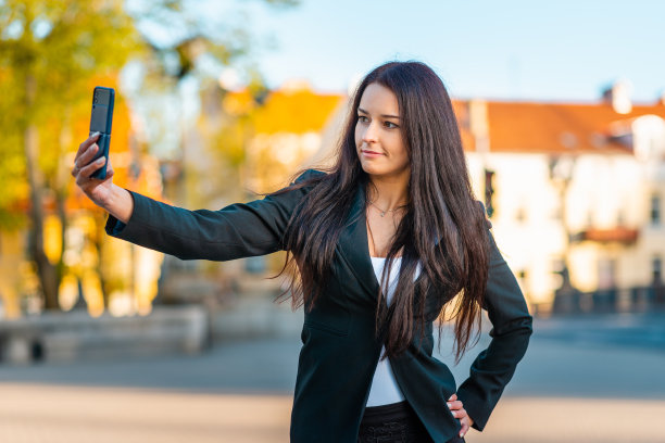 一个年轻美丽的女商人的肖像，穿着西装。女商人在城市里穿梭，视频通话，自拍，拿着电话。新一代的商业，沟通。夏天sunset.Close-up模糊。图片下载