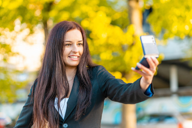 一个年轻美丽的女商人的肖像，穿着西装。女商人在城市里穿梭，视频通话，自拍，拿着电话。新一代的商业，沟通。夏天sunset.Close-up模糊。图片下载