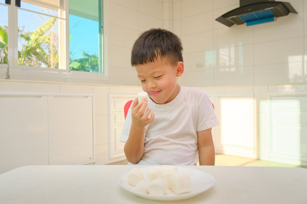 可爱有趣的亚洲小男孩坐在厨房里，家里有棉花糖，不健康的孩子零食图片下载