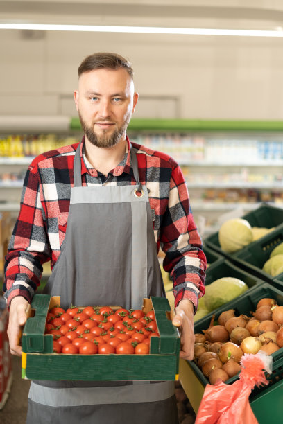 快乐的男性超市工作人员的肖像手里拿着新鲜有机蔬菜的盒子，看着相机和微笑。年轻人吃有机食品图片下载