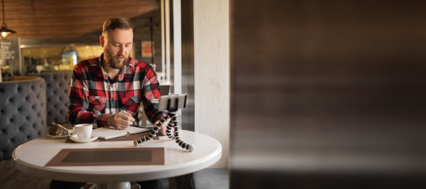 蓄着胡子的学生或商人在三脚架上用智能手机录制直播视频，在笔记本上做笔记，横幅上展示和评论产品图片下载