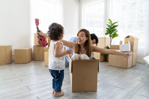 兴高采烈的父母带着蹒跚学步的女儿在纸箱里玩耍，他们搬进了新家，背景是纸箱图片下载