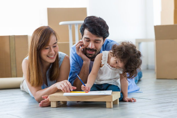 快乐的爸爸和妈妈躺在地板上教蹒跚学步的小女孩画画或在家里用彩色铅笔写书。父亲和母亲与小女儿在客厅共度时光图片下载