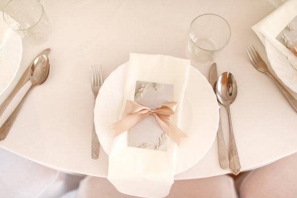婚礼餐桌上的白色盘子，玻璃杯和银餐具。样板空白与粉红色丝带在盘子上图片下载