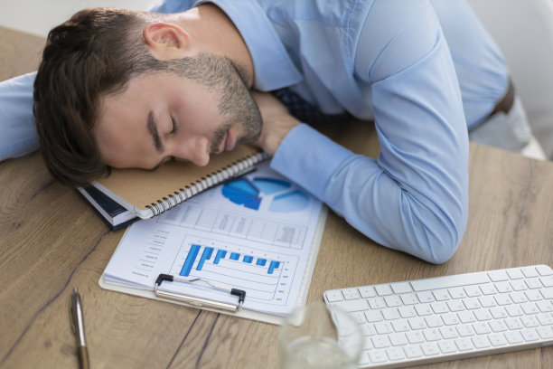 疲惫的年轻男性坐在办公室办公桌后面的电脑前睡觉。图片下载