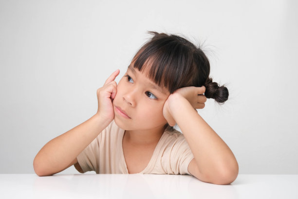 可爱的黑发小女孩坐在一张白色背景的桌子旁，摆出深思熟虑的姿势。图片下载
