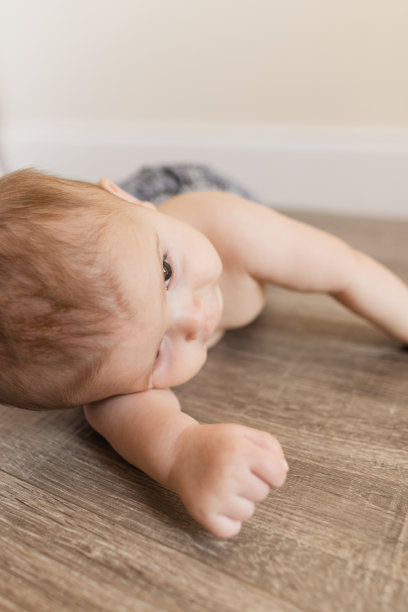 一个24周大的男婴穿着蓝色牛仔牛仔裤和没有衬衫，躺在一个明亮的家里的木地板上图片下载