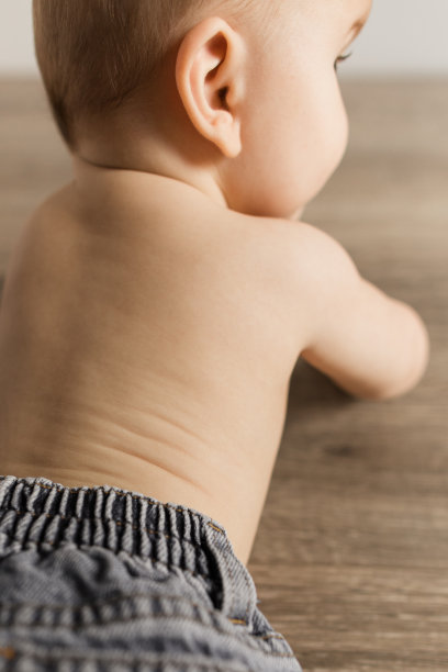 一个24周大的男婴穿着蓝色牛仔牛仔裤和没有衬衫，躺在一个明亮的家里的木地板上图片下载