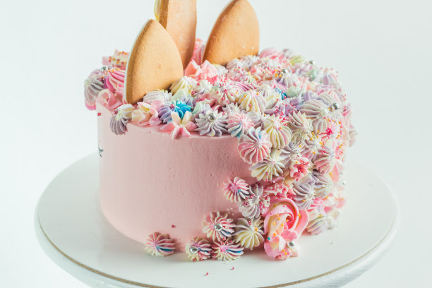 姜饼饼干放在粉红色的生日蛋糕上，上面装饰着奶油芝士花。白色背景的彩色蛋糕送给小女孩图片下载