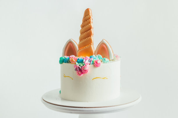 生日蛋糕上的独角兽姜饼，上面装饰着奶油芝士花。白色背景的彩色蛋糕送给小女孩图片下载