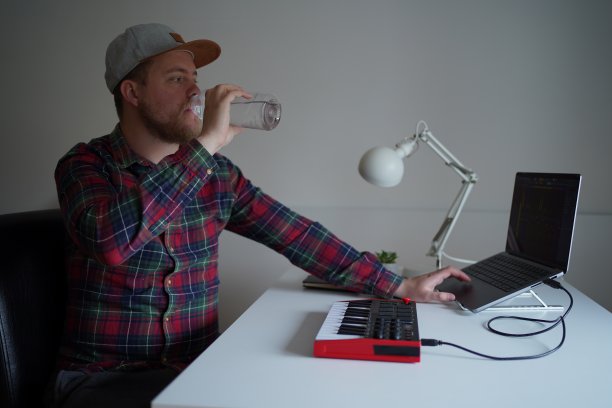 年轻的音乐家在家庭工作室工作，在线为客户和饮用水图片下载