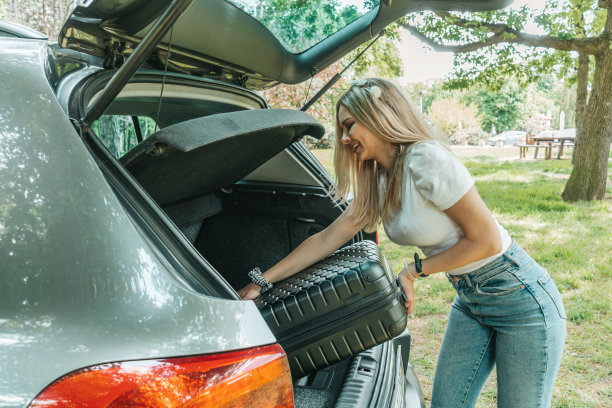 年轻女子把她的手提箱装进汽车行李箱。图片下载