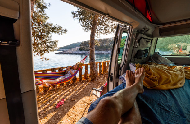 赤脚男人在露营车里放松，而女人在吊床上拿着手机图片下载