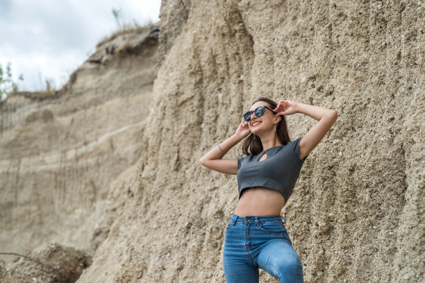 运动女孩穿着上衣和牛仔裤在夏天的沙质山采石场摆姿势图片下载