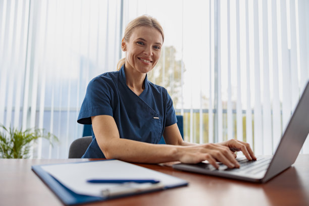 微笑的医生治疗师工作笔记本电脑在她的医疗办公室预约和看相机图片下载