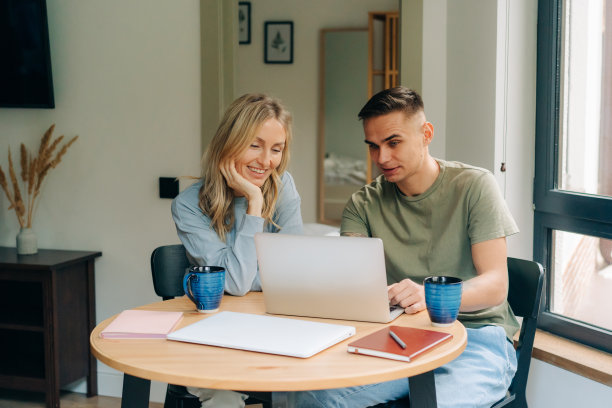 年轻的男女坐在家里的桌子前用笔记本电脑工作。图片下载