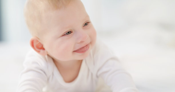 一个可爱的白人婴儿躺在明亮的房间里的特写。一个快乐可爱的金发小男孩的肖像独自看着镜头和微笑的白色背景。现代的童年图片下载