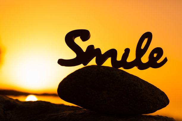 黑色木制字母微笑的剪影在一个真正的日出面前的石头图片下载