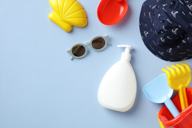 儿童防晒乳瓶设计。蓝色的桌子上平铺着婴儿防晒霜、太阳镜、巴拿马草帽、沙模。图片下载