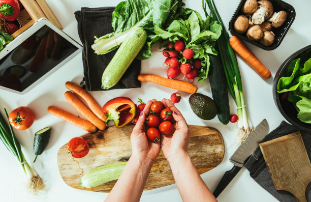 特写照片的女人手拿着樱桃番茄上方满是有机蔬菜的桌子图片下载