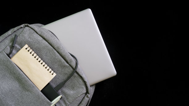 灰色纺织双肩包与笔记本电脑，记事本和外部ssd或电源银行的黑色背景。背包概念为高中生或经理。自由的空间为铭文图片下载