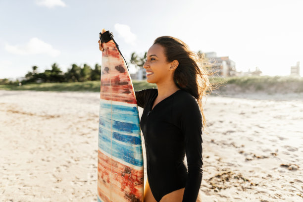 年轻的冲浪女子的肖像在海滩上拿着她的冲浪板图片下载