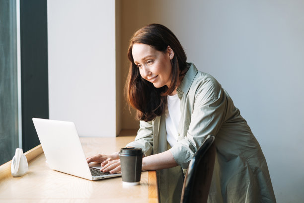 成年微笑的深褐色商业女性40年的长发在时尚的衬衫在咖啡馆的笔记本电脑上工作图片下载