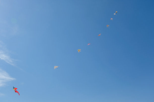 五彩缤纷的风筝排成一行，映衬着深蓝的天空。图片下载