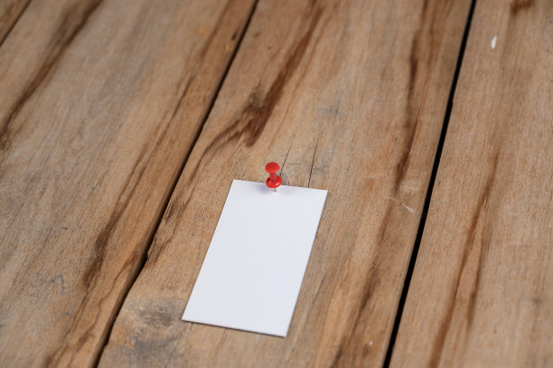 一张木制背景的空白名片。用推杆把一个白纸长方形钉在旧木板上。有选择性的重点。图片下载