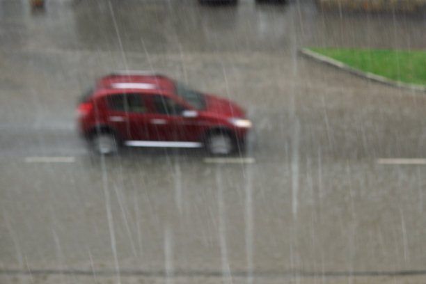 在暴雨中，一辆模糊的红色汽车行驶在满是泥泞水坑的洪水道路上。图片下载