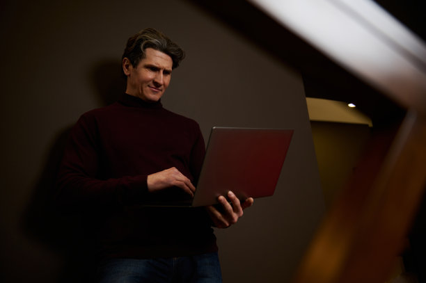 有吸引力的英俊成熟的欧洲男人在深棕色的墙壁背景下远程工作在笔记本电脑上。商人，企业家，文案，自由记者。在线工作概念图片下载