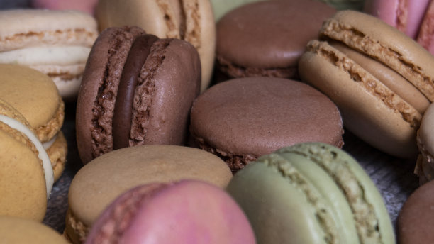 全帧图像堆多色马卡龙填充调味黄油奶油，香草，柠檬，咸焦糖，巧克力，草莓和开心果口味的蛋白，木纹背景，重点在前景图片下载