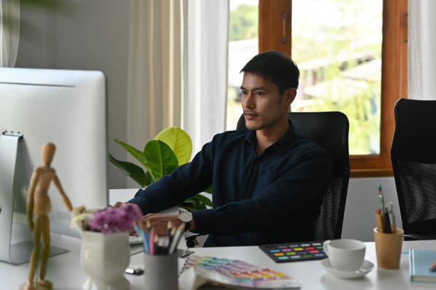 一幅亚洲设计师或创意工作者的肖像，坐在办公室里，在电脑上进行艺术、设计和商业概念的设计。图片下载