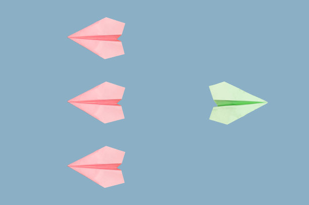 粉红色的折纸飞机与突出的绿色飞机在蓝色背景上飞向相反的方向。新理念、独立、独特、个性、创新理念。图片下载