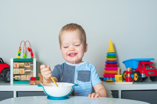 蹒跚学步的小男孩用勺子吃饭，身上沾满了食物。宝宝食品，食物过敏，自行喂养....图片下载