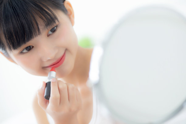 美丽的亚洲年轻女性涂口红的嘴红色，美丽的女孩看着镜子化妆化妆品与唇优雅，化妆与性感的女性，护肤和健康的概念。图片下载