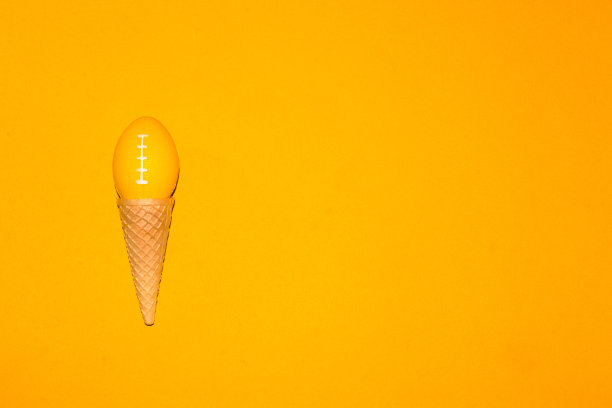美式足球用球代替冰淇淋球，创意艺术设计，黄色背景上缓慢的冰淇淋图片下载