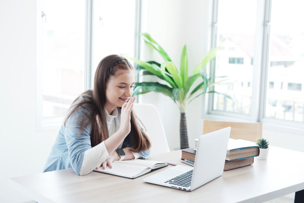 微笑的白人女学生正在家里用笔记本电脑进行在线学习和电话会议。她在家用笔记本电脑和老师聊天、打招呼。家庭教育和技术概念。图片下载