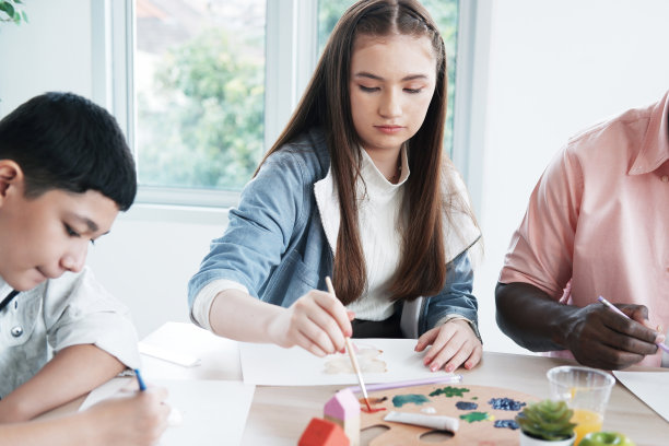 图为，在国际学校的教室里，满面笑容的白人和非洲学生正在用画笔和水彩画画画。艺术家概念教育。图片下载