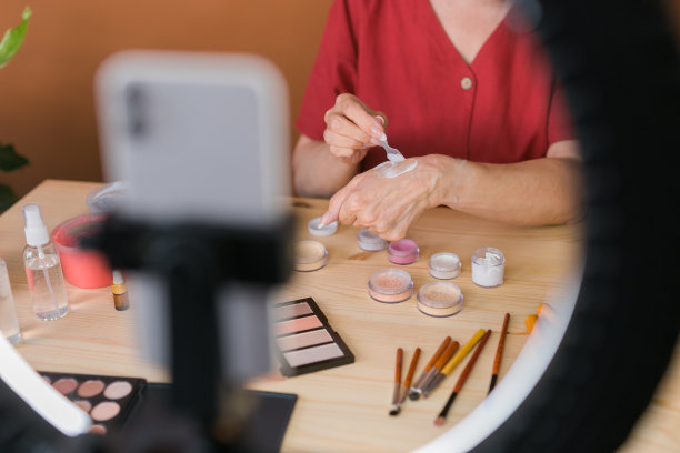 中年女性美妆博主或网红在家里的房间里用化妆产品录制视频。使用环形灯和智能手机图片下载