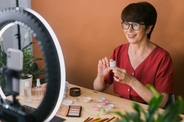 中年女性美妆博主或网红在家里的房间里用化妆产品录制视频。使用环形灯和智能手机图片下载